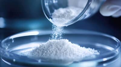 White medicinal powder being poured out of a beaker in a lab