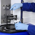Hands in gloves adding a container into the LabRAM II for mixing